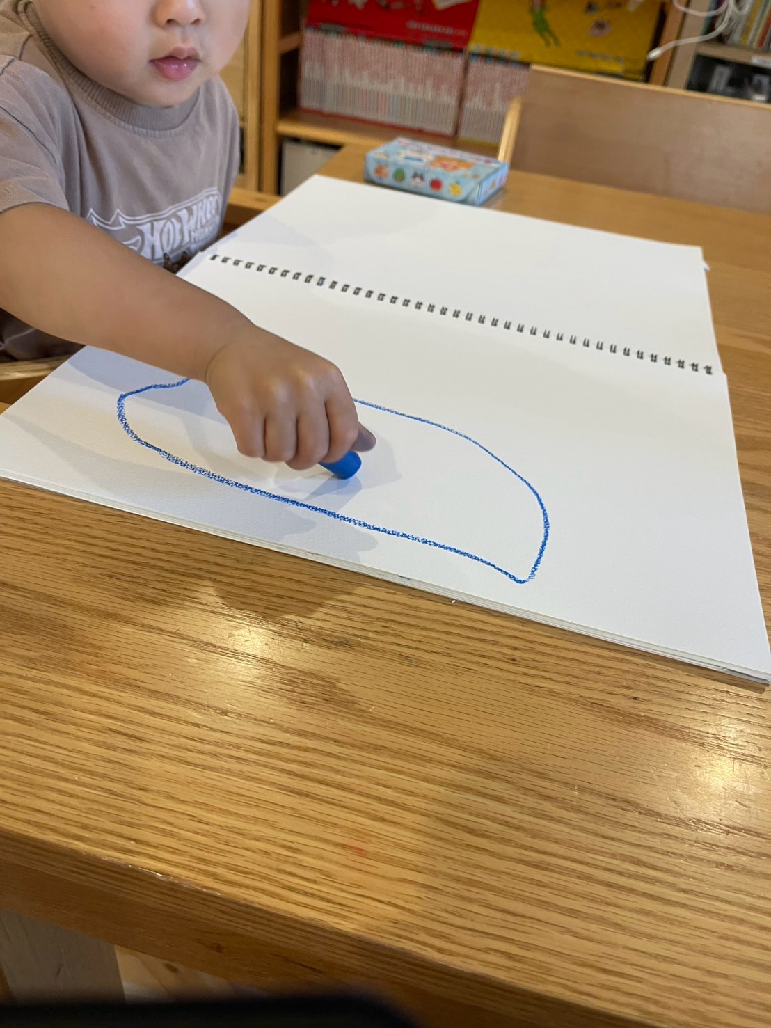 青いクレヨンでスケッチブックにお絵描きをするお子さま